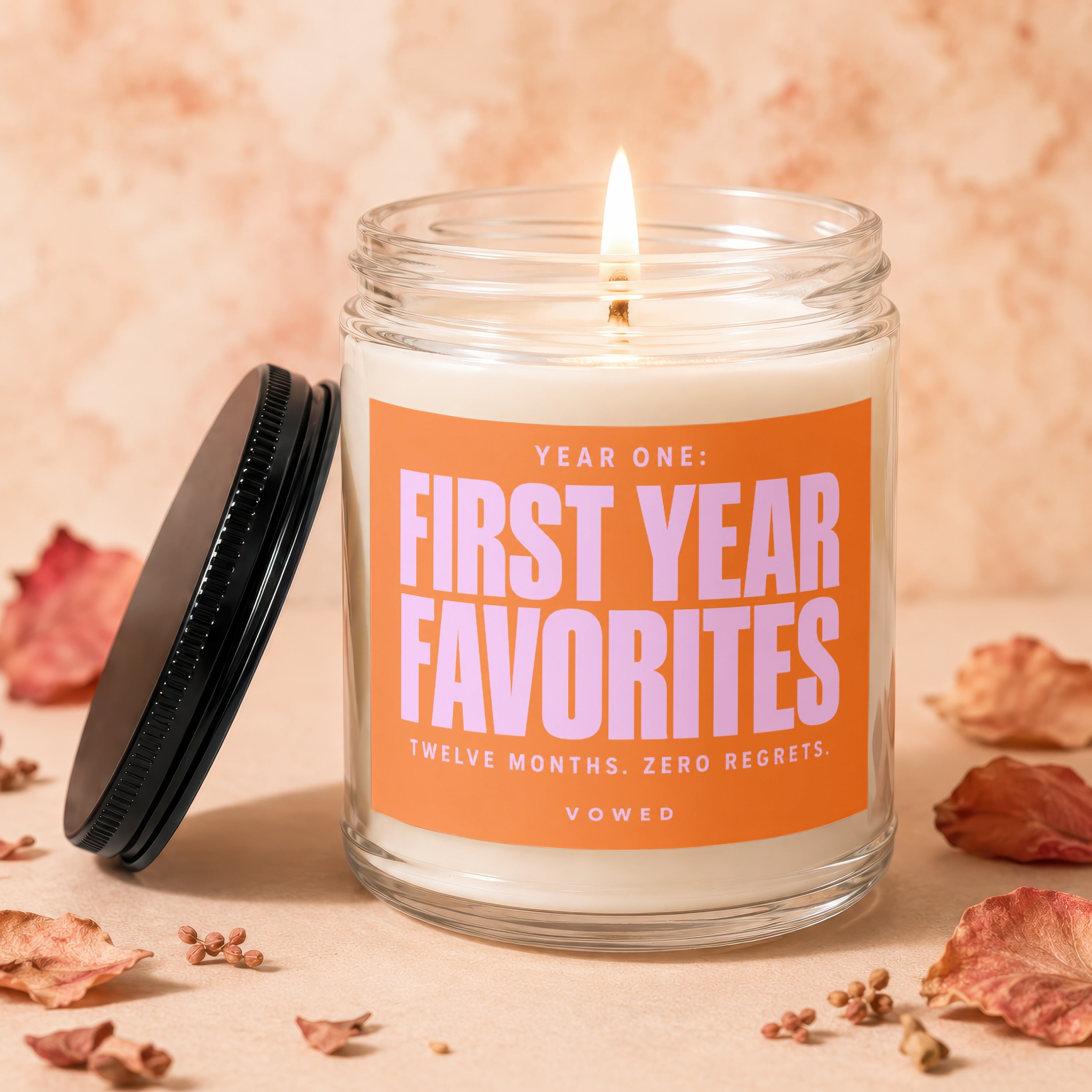Jar candle with lit wick, orange label reading "Year One: First Year Favorites Twelve Months. Zero Regrets. vowed."