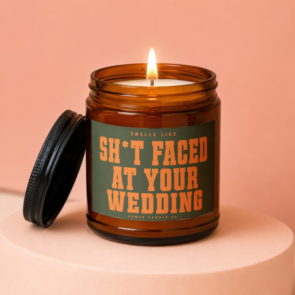 Amber jar candle with lit wick and black lid. Text reads "Smells Like Sh*t Faced At Your Wedding".