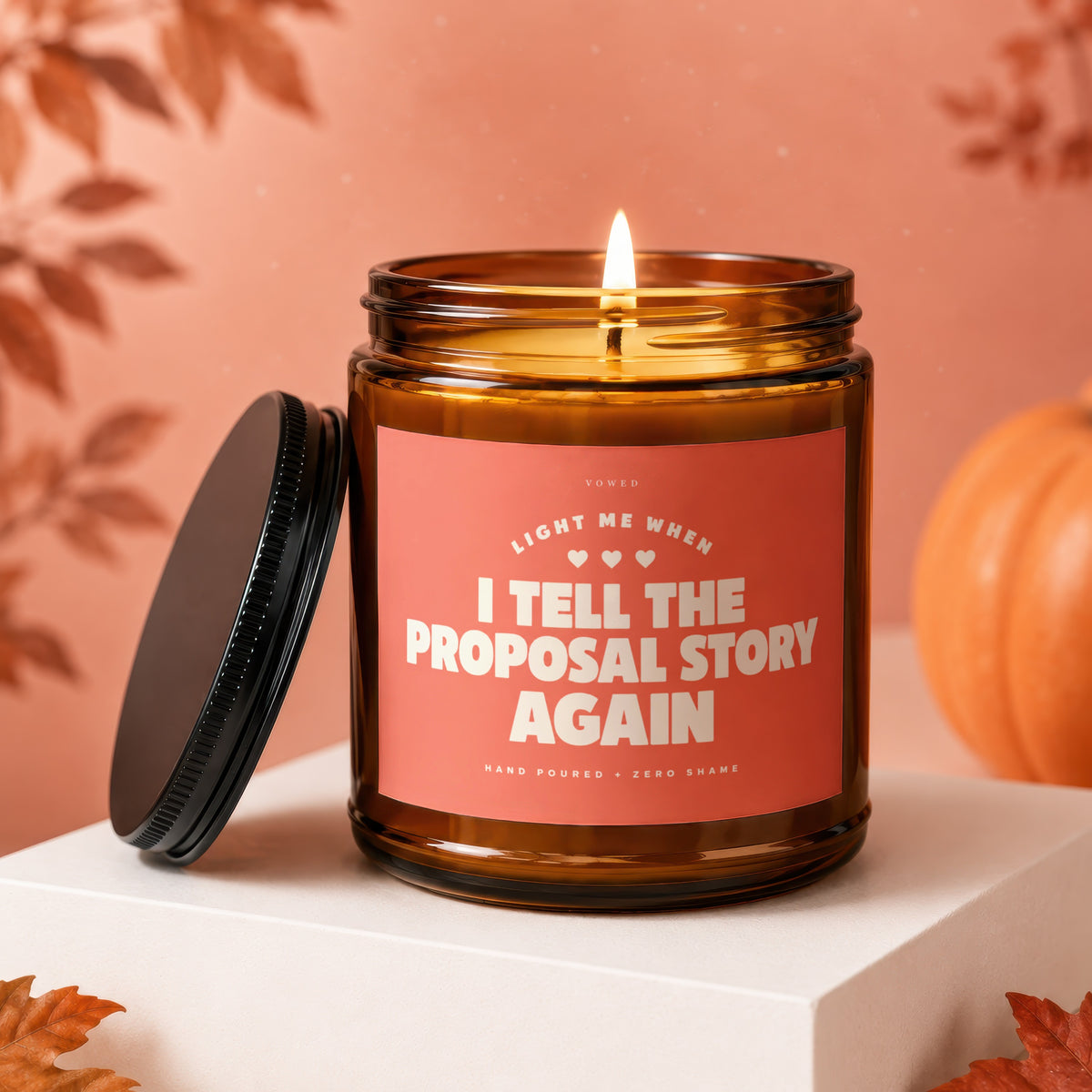 Amber candle with pink label reading "Light Me When I Tell The Proposal Story Again".