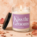 Glass candle with a lit wick and "Kiss the Grooms VOWED" text on a lavender label.
