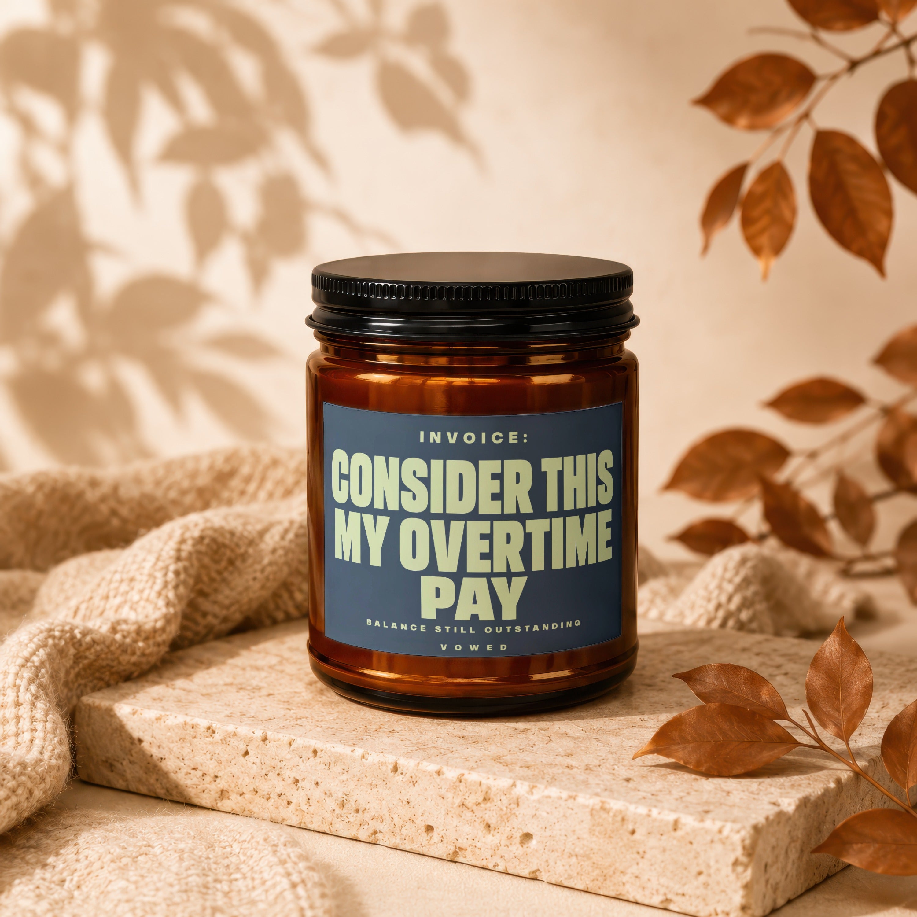Amber jar candle with a blue label reading "INVOICE: CONSIDER THIS MY OVERTIME PAY".
