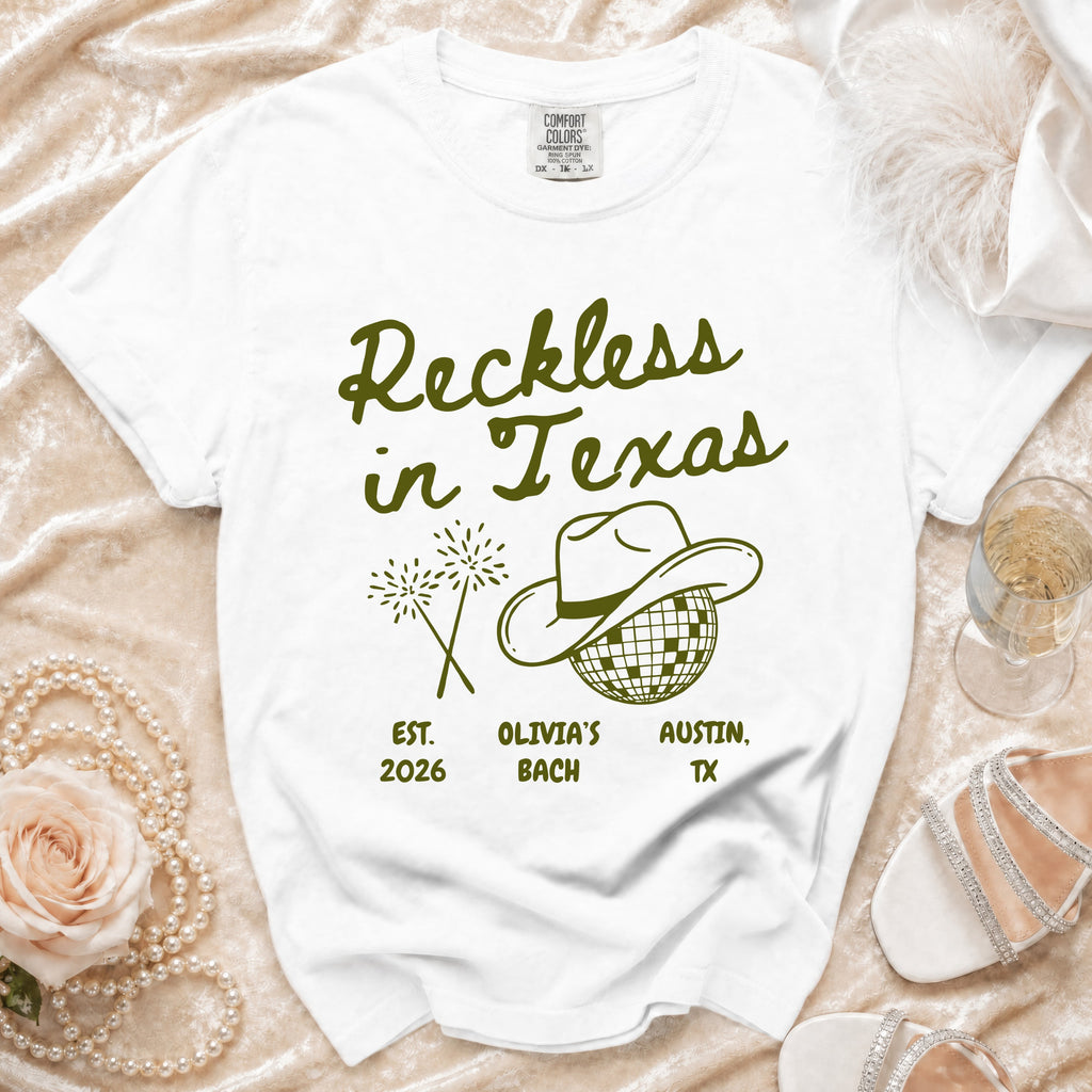 White t-shirt with "Reckless in Texas" text, cowboy hat, and fireworks.