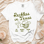 White t-shirt with "Reckless in Texas" text, cowboy hat, and fireworks.