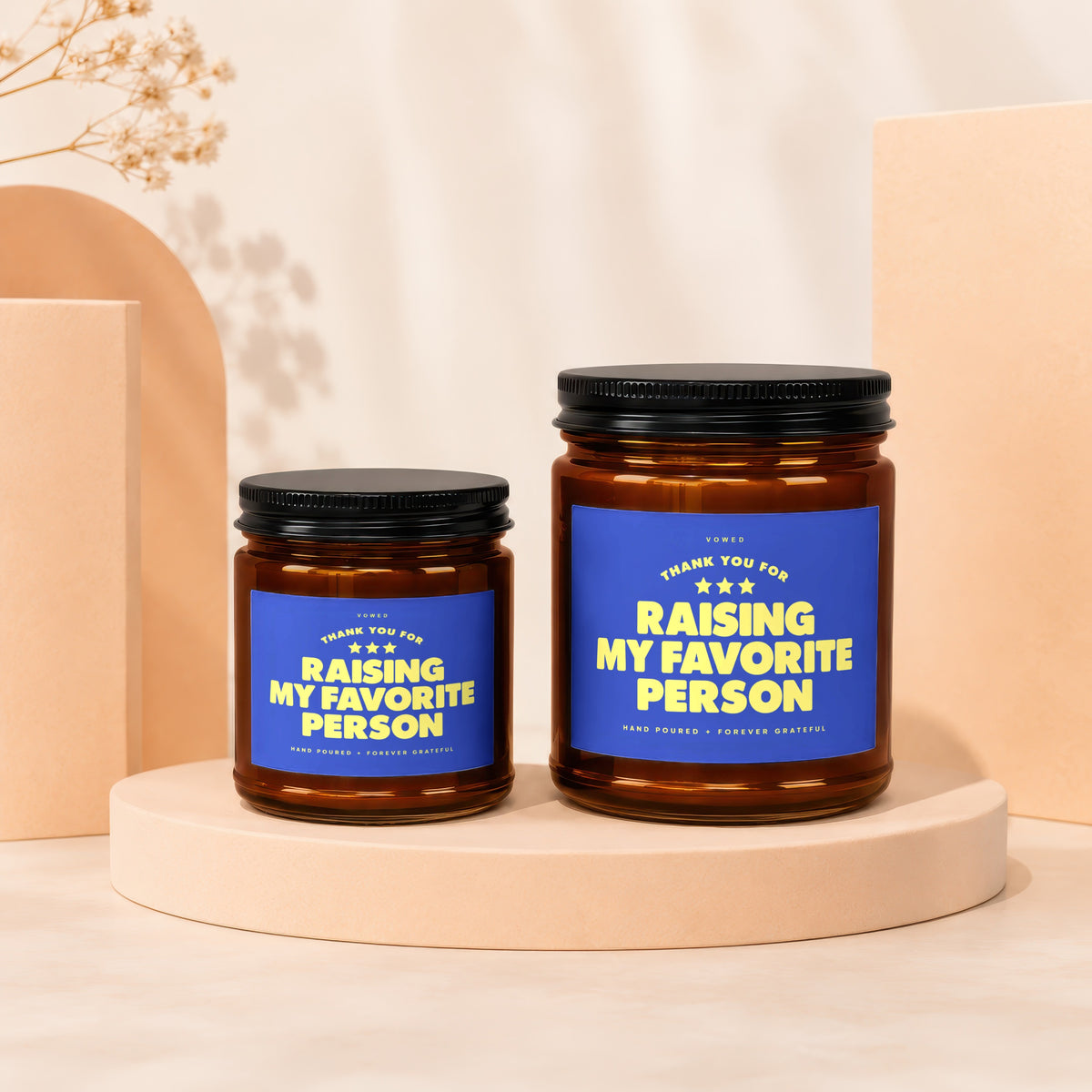 Two amber glass candles with black lids, featuring blue labels with yellow text.