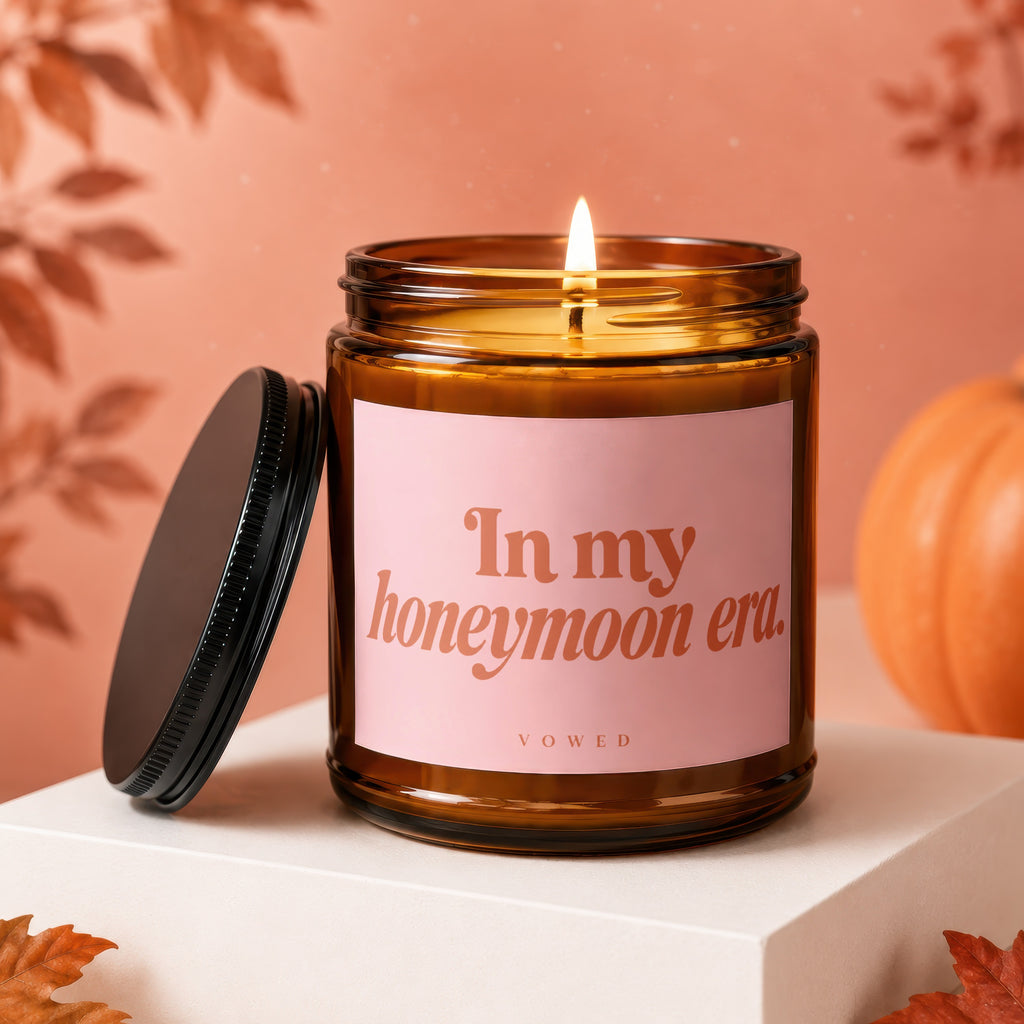 Amber glass candle with lit wick, pink label reads "In my honeymoon era.".
