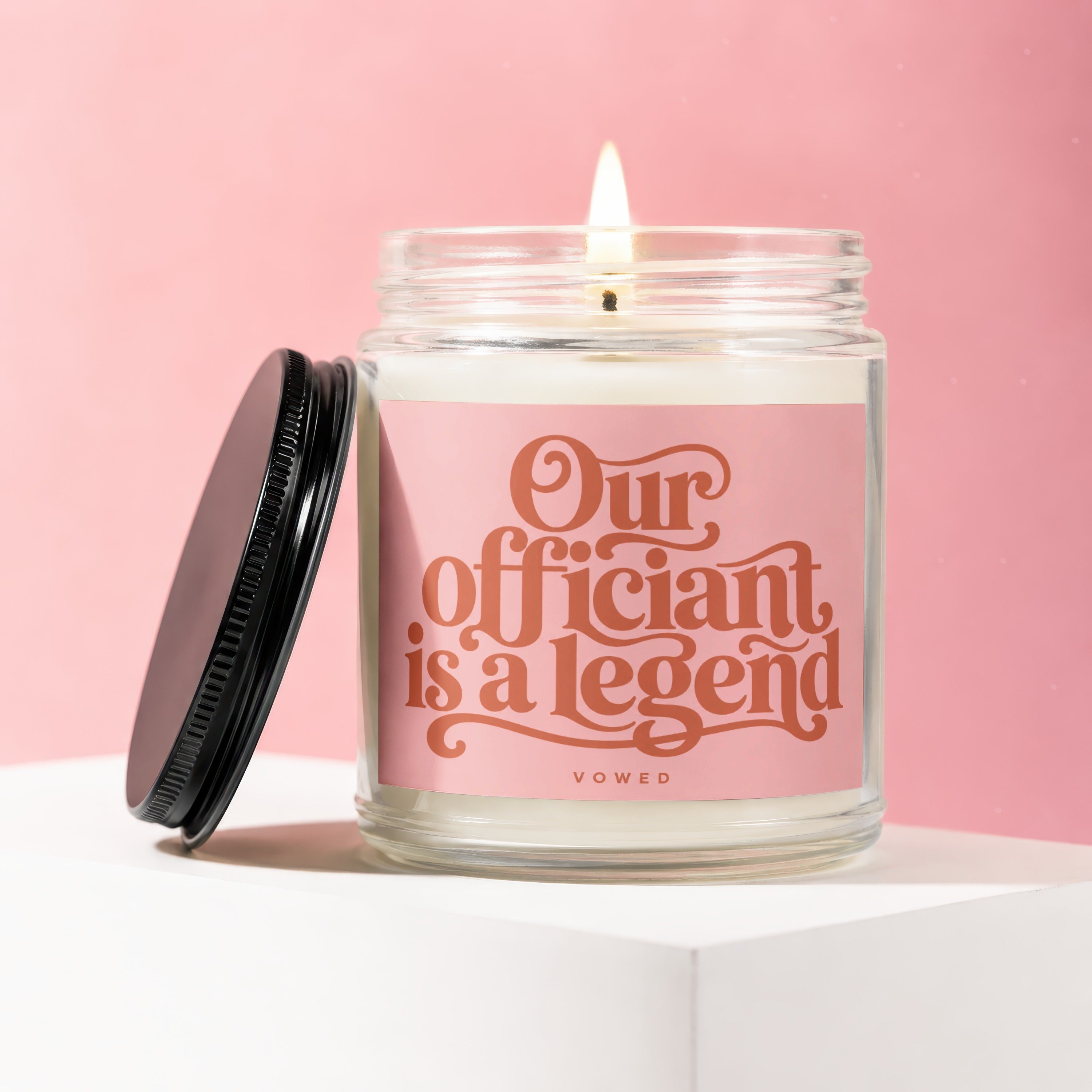 Glass jar candle with pink label that reads "Our officiant is a legend"
