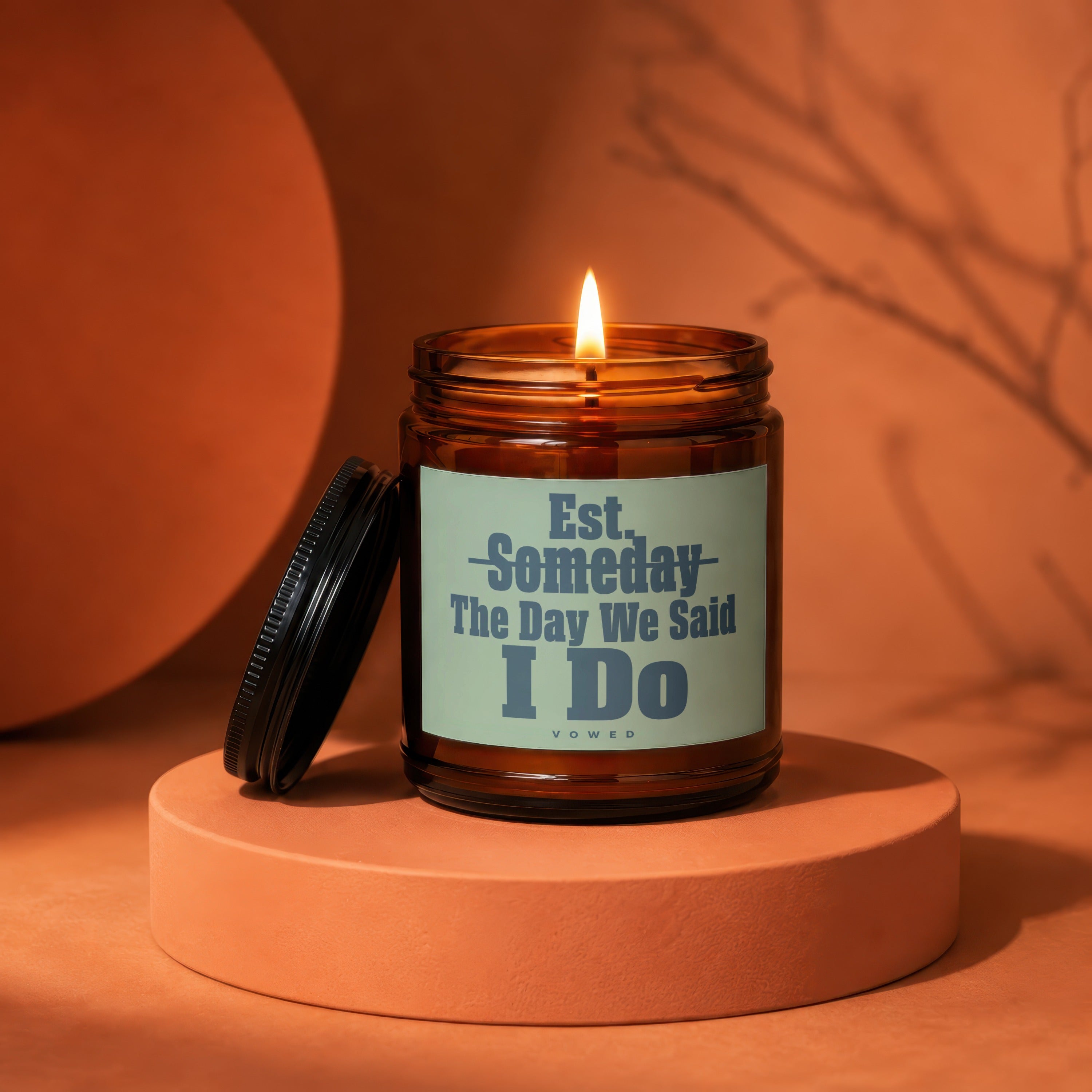 Amber glass candle with lit flame and label that reads "Est. Someday The Day We Said I Do".