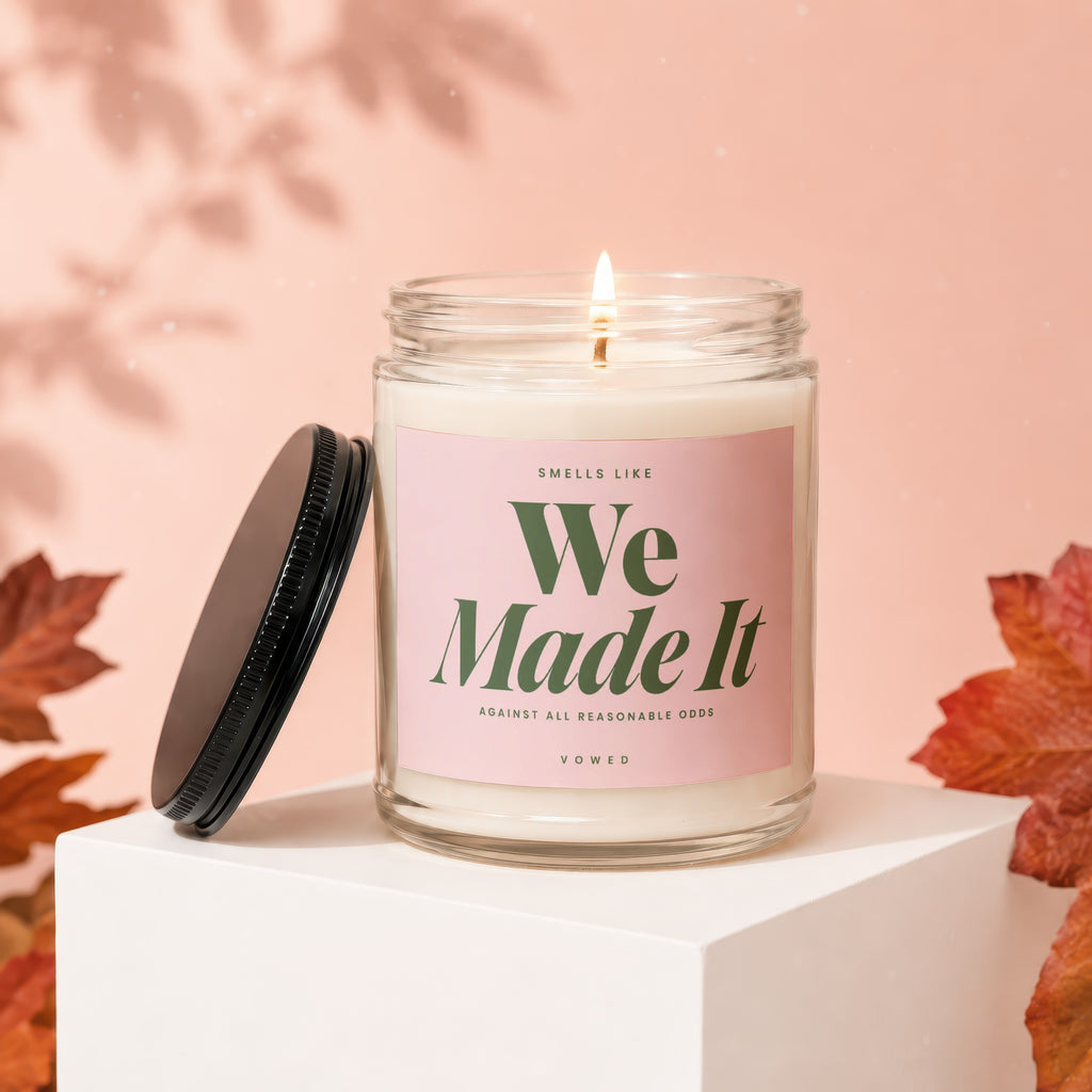 Lit candle with pink label reading "Smells Like We Made It" in green text.