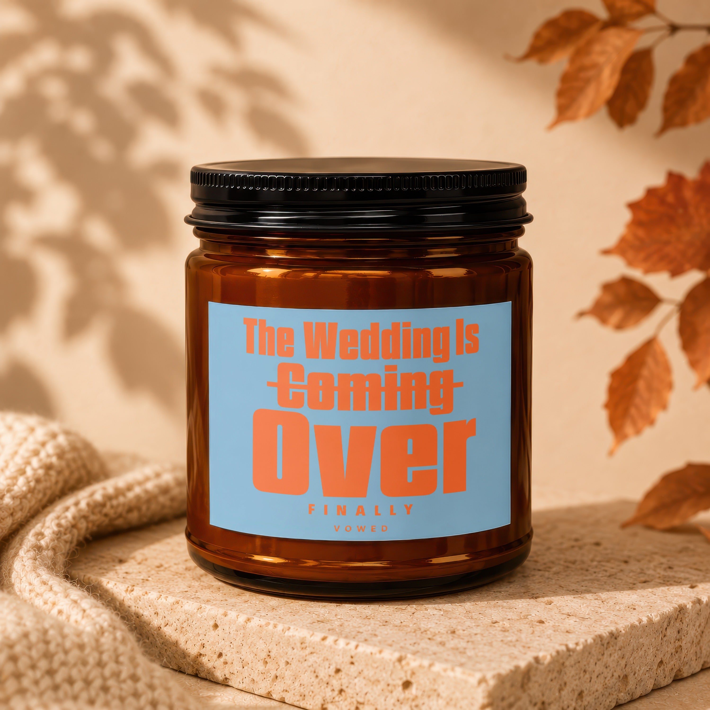 Brown candle in amber glass jar with black lid, label reads "The Wedding Is Coming Over"