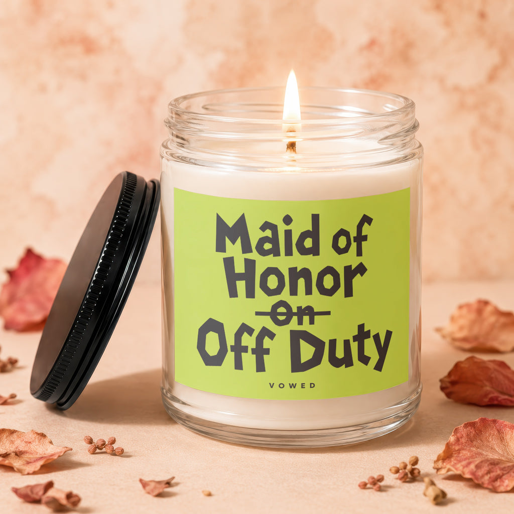 Lit candle in a glass jar with black lid, reading "Maid of Honor on Off Duty."