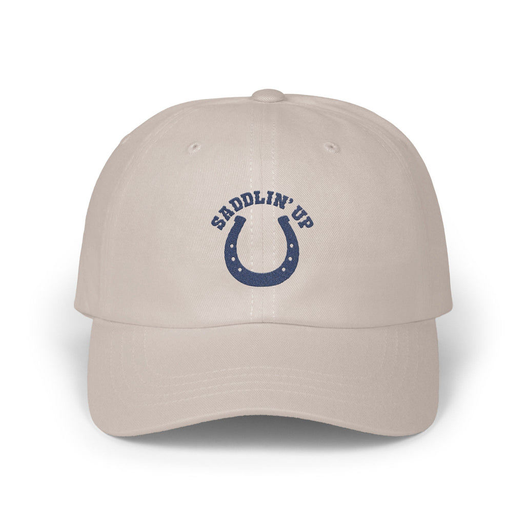 Light beige baseball cap featuring an embroidered blue horseshoe design with the text SADDLIN UP.