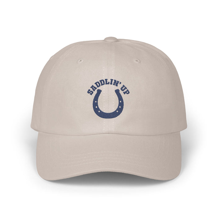 Light beige baseball cap featuring an embroidered blue horseshoe design with the text SADDLIN UP.