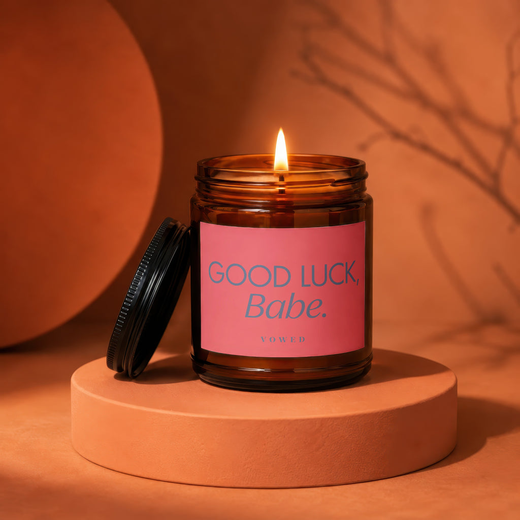 Lit amber glass candle with pink label reading "GOOD LUCK, Babe."