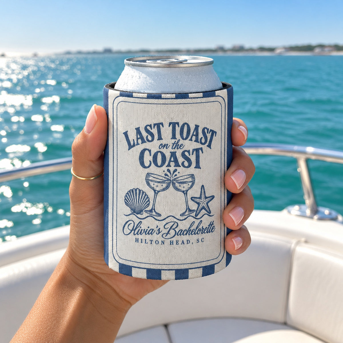 Hand holding a can in a Blue Jean Last Toast On The Coast can cooler on a boat