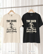 Ivory bride shirt printed in Black next to a Black crew shirt printed in ivory, Forever Starts With A Howdy tees
