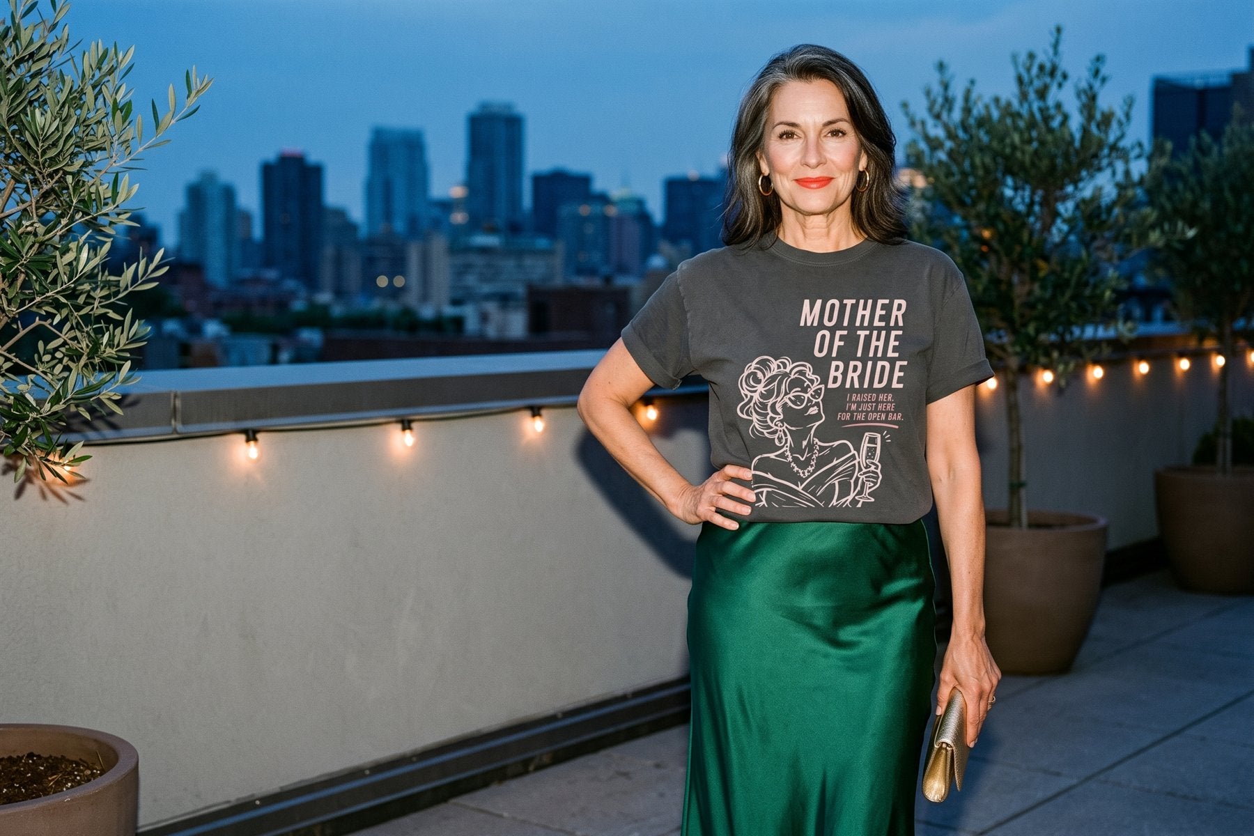 Mother of the bride in the Open Bar tee and an emerald satin skirt on a city rooftop at dusk